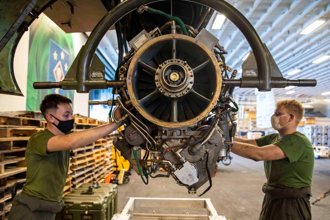 Two Marines stand on either side of an aircraft engine.