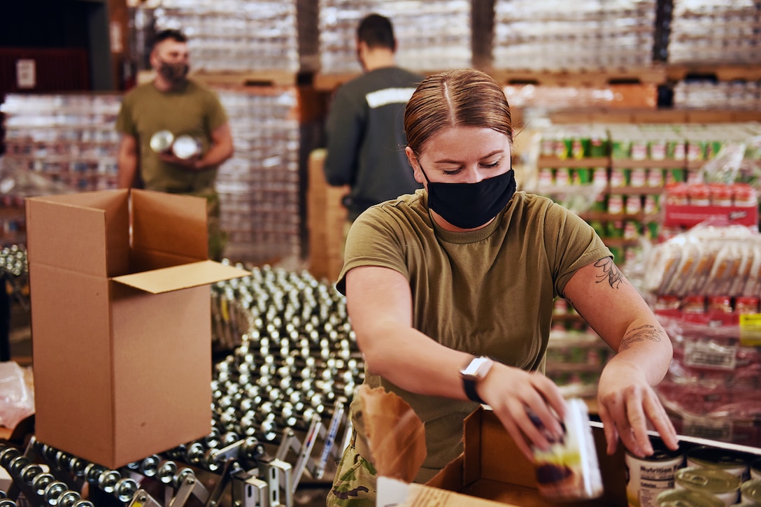 A soldier wearing a face mask helps prepare pallets of food orders for distribution to the community.