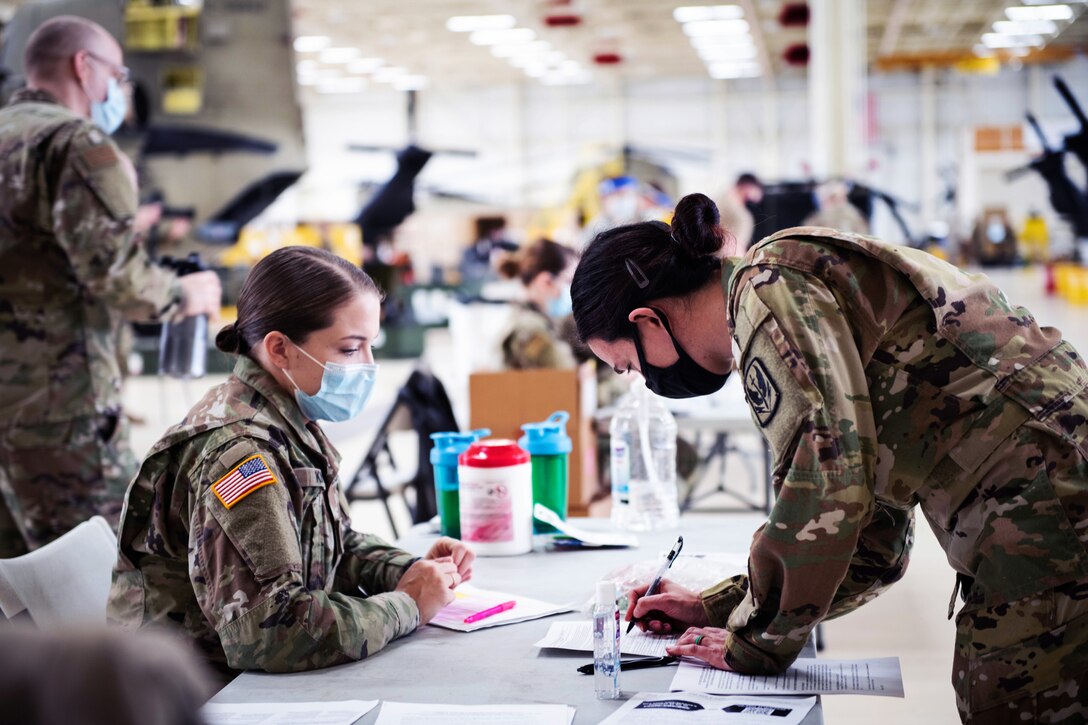 An Army soldier wearing a face mask watches as another soldier wearing a face mask fills out paperwork prior to getting a COVID-19 vaccine.