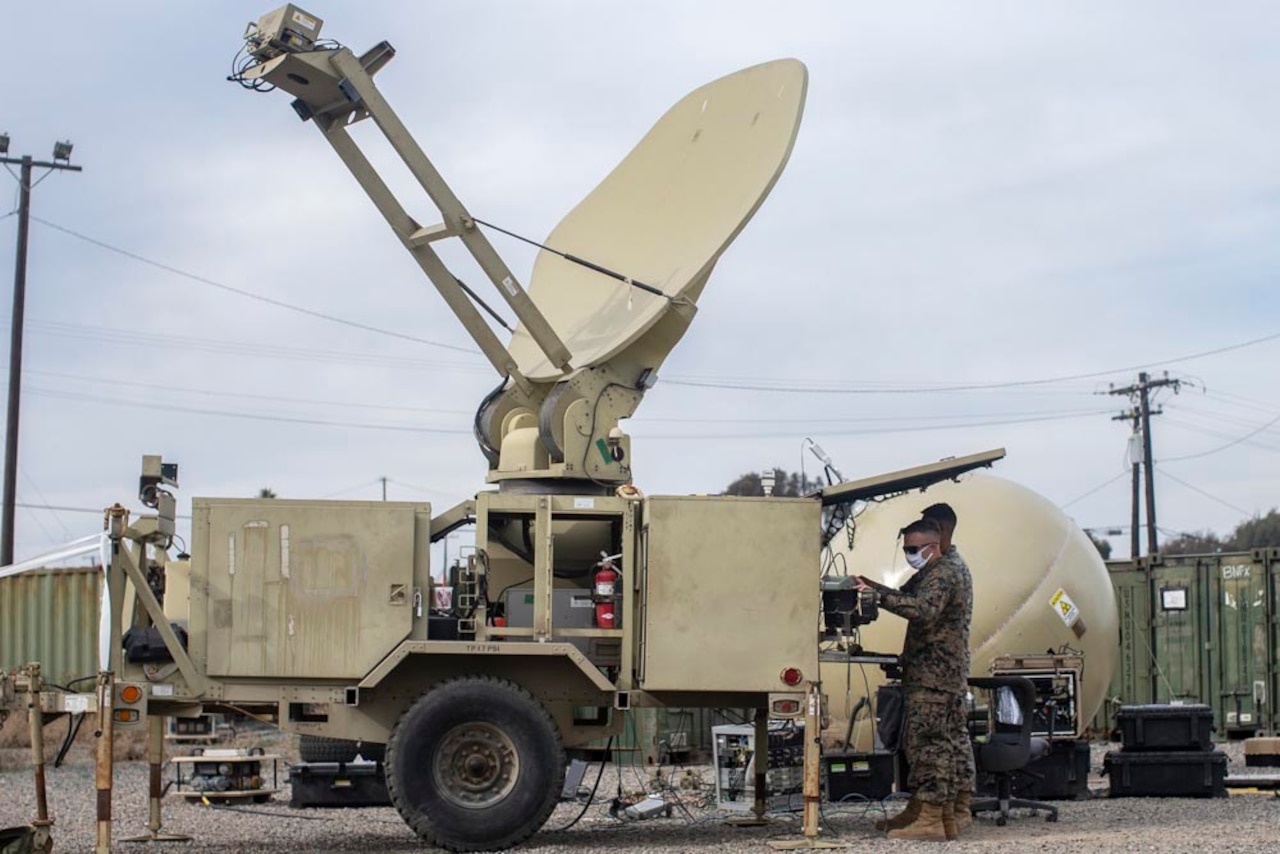 Two men dressed in military uniforms work outside on communications gear.