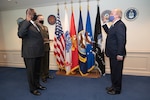 Defense Secretary Lloyd J. Austin III stands next to a man holding up his right hand facing another man.