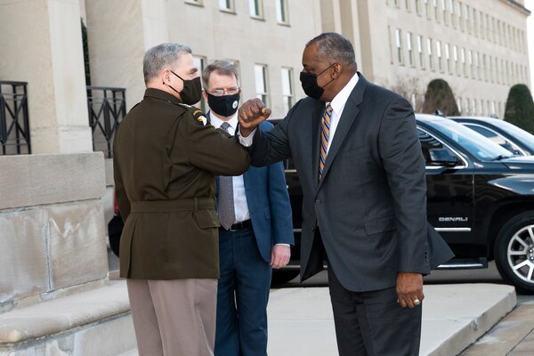 Two men wearing protective face masks bump elbows in front of the Pentagon entrance.