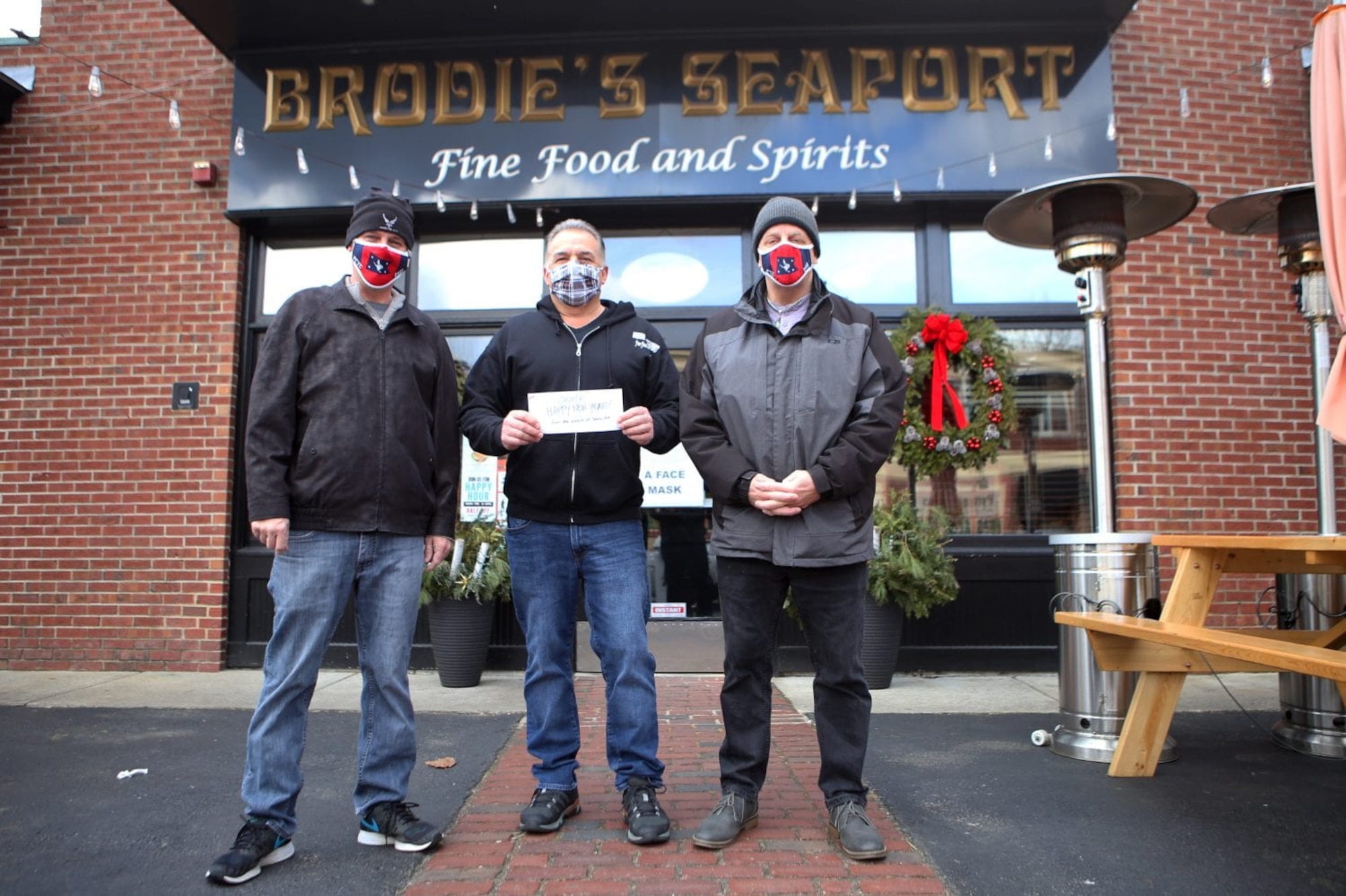 Scott Sheehan, left, 66th Civil Engineering Division environmental engineer, presents a $100 donation to Brodie’s Seaport bartender Chuck Rollins alongside local resident Mark Roberts in Salem, Mass., Jan. 18. Sheehan and Roberts have raised more than $7,500 for Salem restaurant managers, servers and bartenders. (Courtesy photo by Olivia Falcigno/The Daily Item)