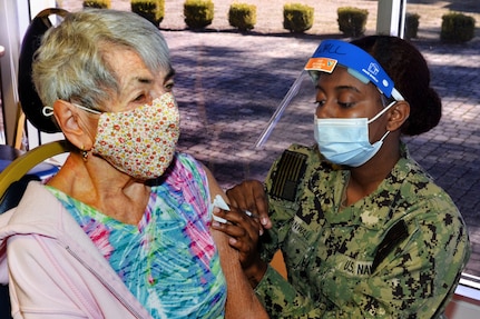 A soldier wearing a face mask administers a COVID-19 vaccine to an elderly woman.