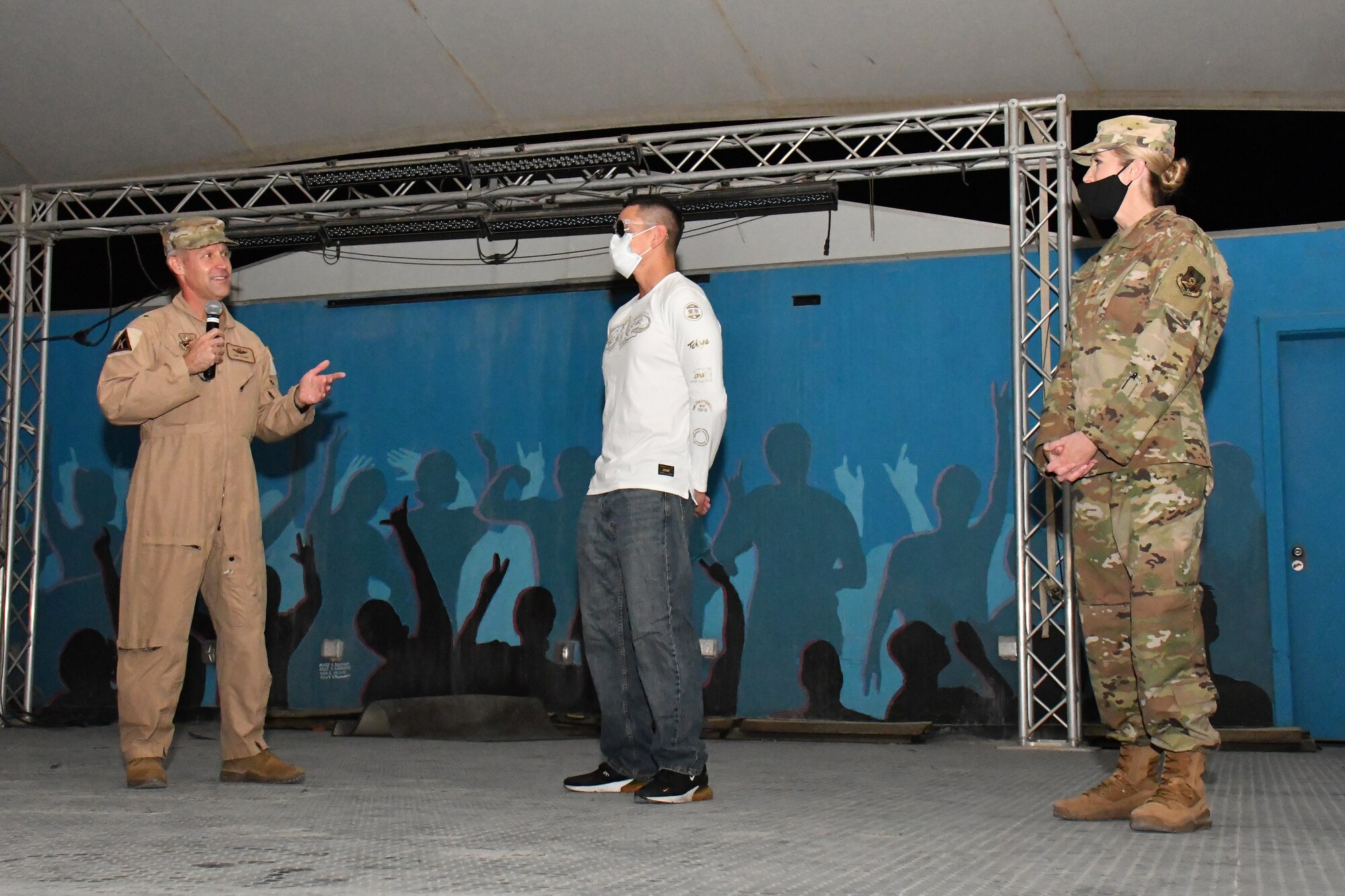 379 AEW commander and command chief stand on stage to either side of Airman accepting winning trophy.