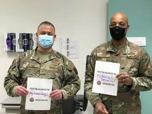 Two men hold up signs stating why they got vaccinated, for family and community