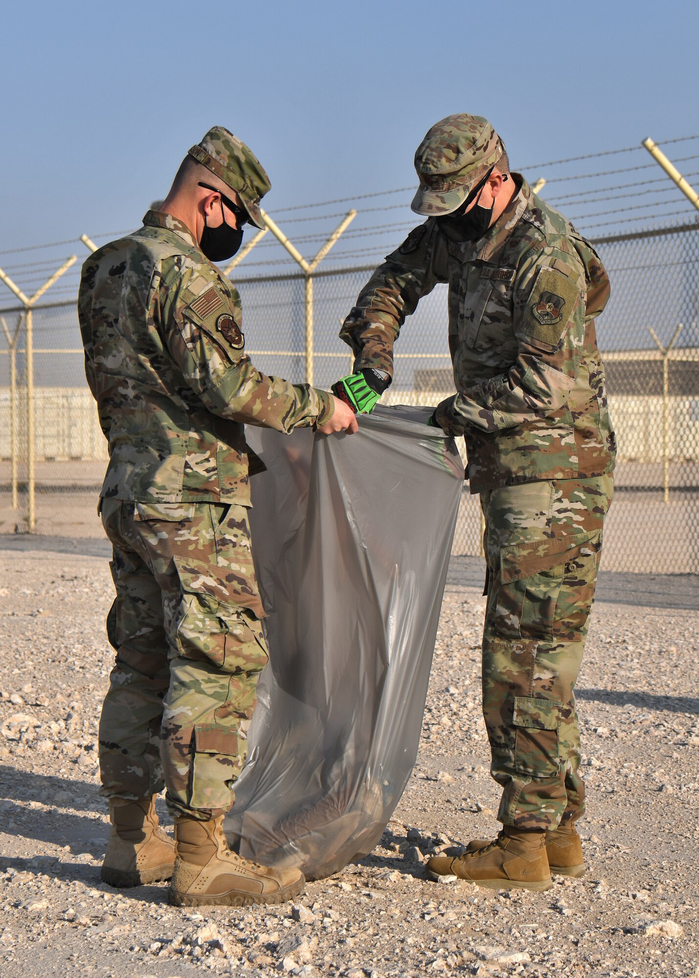 Two Airmen filling a trash bag.