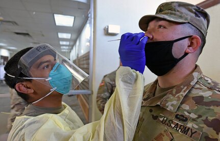 Pvt. Daniel Flores with Company A, 232nd Medical Battalion, uses a cotton swap to test Staff Sgt. Jose Gomez with Company A, 264th Medical Battalion, for COVID-19.