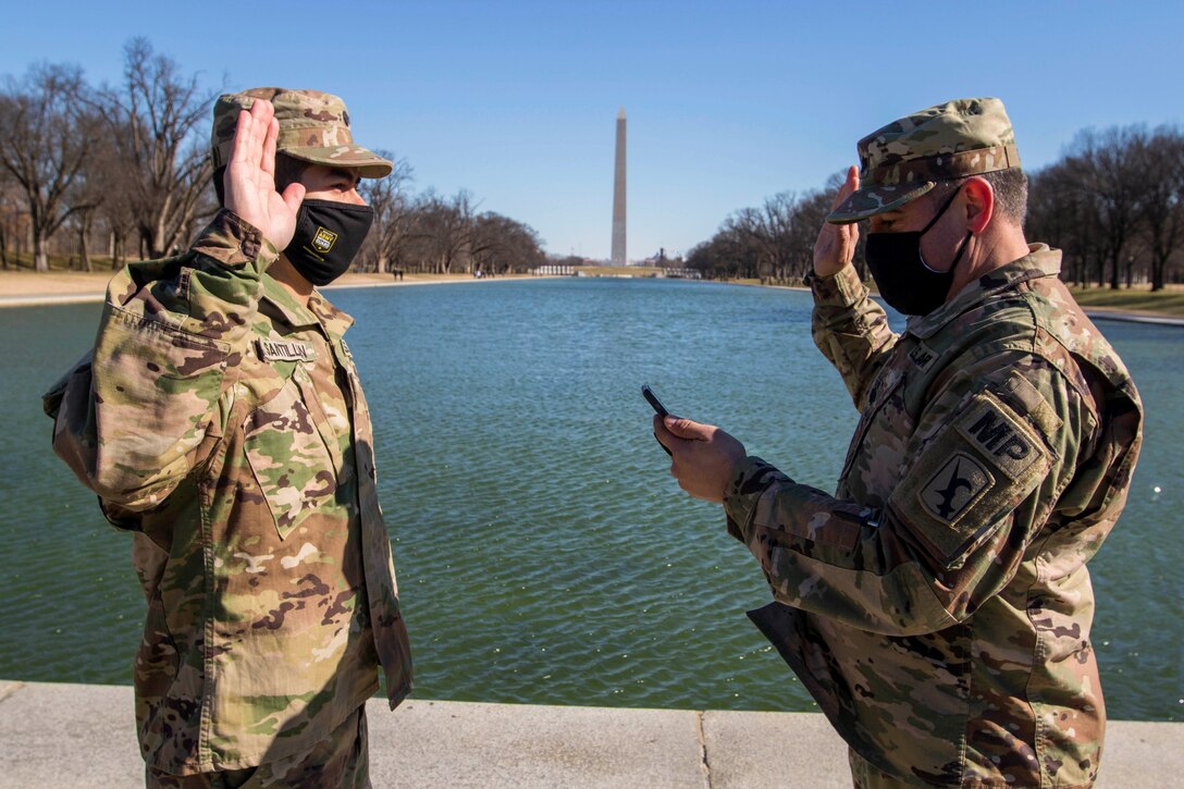 Soldiers face each other while raising their right hands in front of the Washington Monument.