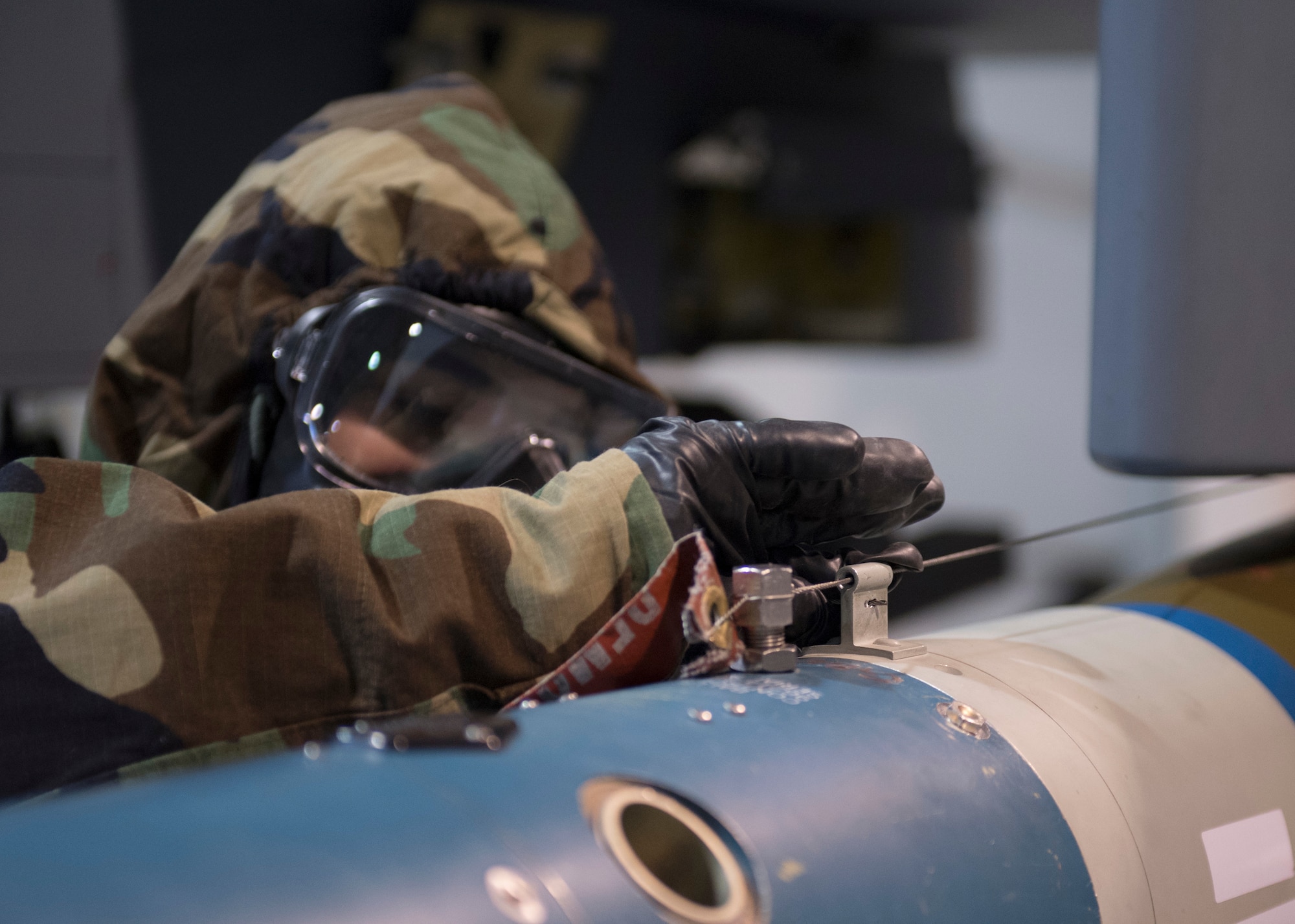 An US Airforce member threads arming wire while wearing chemical, biological, radiological and nuclear equipment.