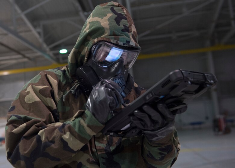 An US Airforce member uses a tablet to check technical order while wearing chemical, biological, radiological and nuclear equipment.
