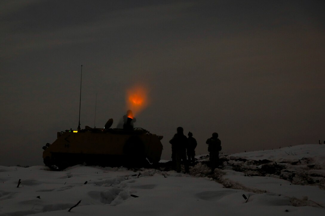 U.S. and Lithuanian soldiers shown in silhouette fire mortars at night and are illuminated by an orange light.