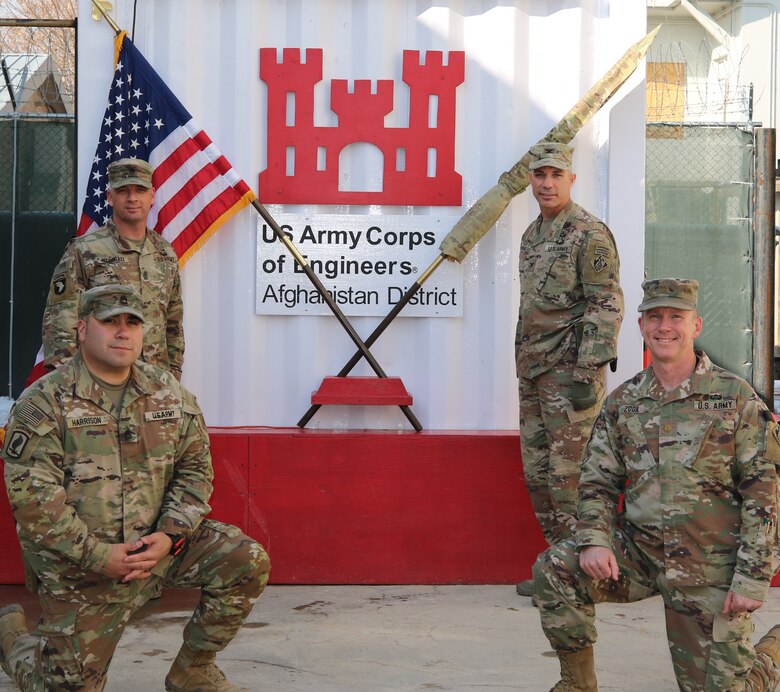 U. S. Soldiers of the U. S. Army Corps of Engineers, Transatlantic Afghanistan District, Bagram Airfield pose in front of the U.S. and USACE command flag after the Casing of the Colors Ceremony. Representing the District are from left, Sergeant First Class Joseph Harrison (kneeling), Sergeant Major Nathan Marshall, Senior Enlisted Leader, COL Mark Geraldi, Afghanistan District Commanding Officer, and Major John Zook (kneeling).