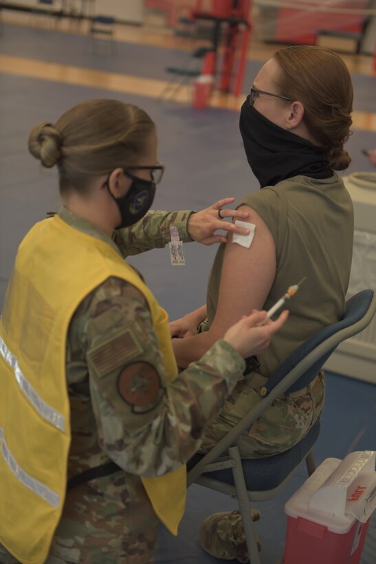 U.S. Air Force Tech. Sgt. Haley Lecomte, 325th Operational Medical Readiness Squadron technician, left, administers the Coronavirus vaccine to Chief Master Sgt. Kati Grabham, 325th Fighter Wing command chief, right, at Tyndall Air Force Base, Florida, Jan. 21, 2021. The vaccine was released as voluntary for active duty personnel based on a U.S. Food and Drug Administration population schema and is a two-dose delivery system. (U.S. Air Force photo by Staff Sgt. Magen M. Reeves)