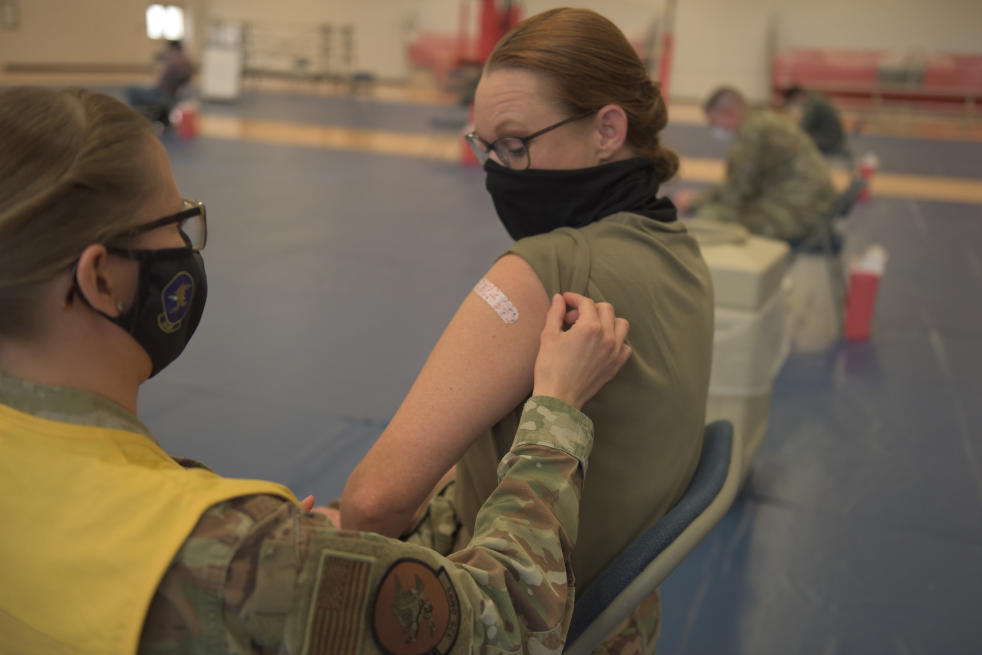 U.S. Air Force Tech. Sgt. Haley Lecomte, 325th Operational Medical Readiness Squadron technician, left, applies a bandage to Chief Master Sgt. Kati Grabham, 325th Fighter Wing command chief, right, after administering the COVID-19 vaccine at Tyndall Air Force Base, Florida, Jan. 21, 2021. The vaccine was initially distributed by the U.S. Food and Drug Administration and is covered by the military healthcare system. (U.S. Air Force photo by Staff Sgt. Magen M. Reeves)