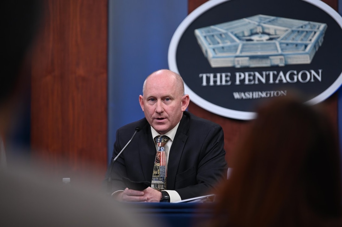 A man speaks into a microphone. A sign behind him indicates that he is at the Pentagon.