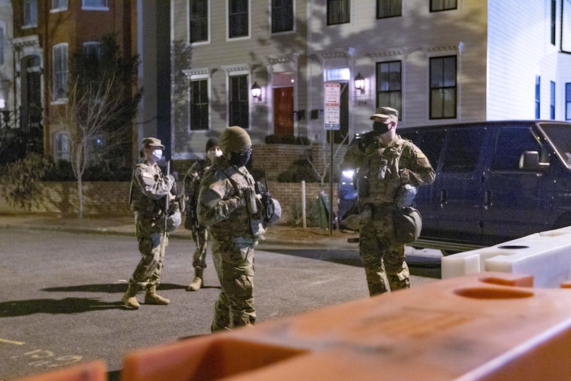 Guardsmen walk down a street at night.