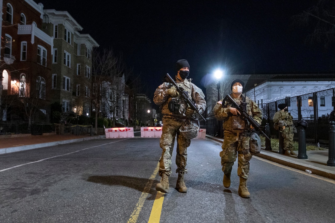 Guardsmen walk down a street at night.