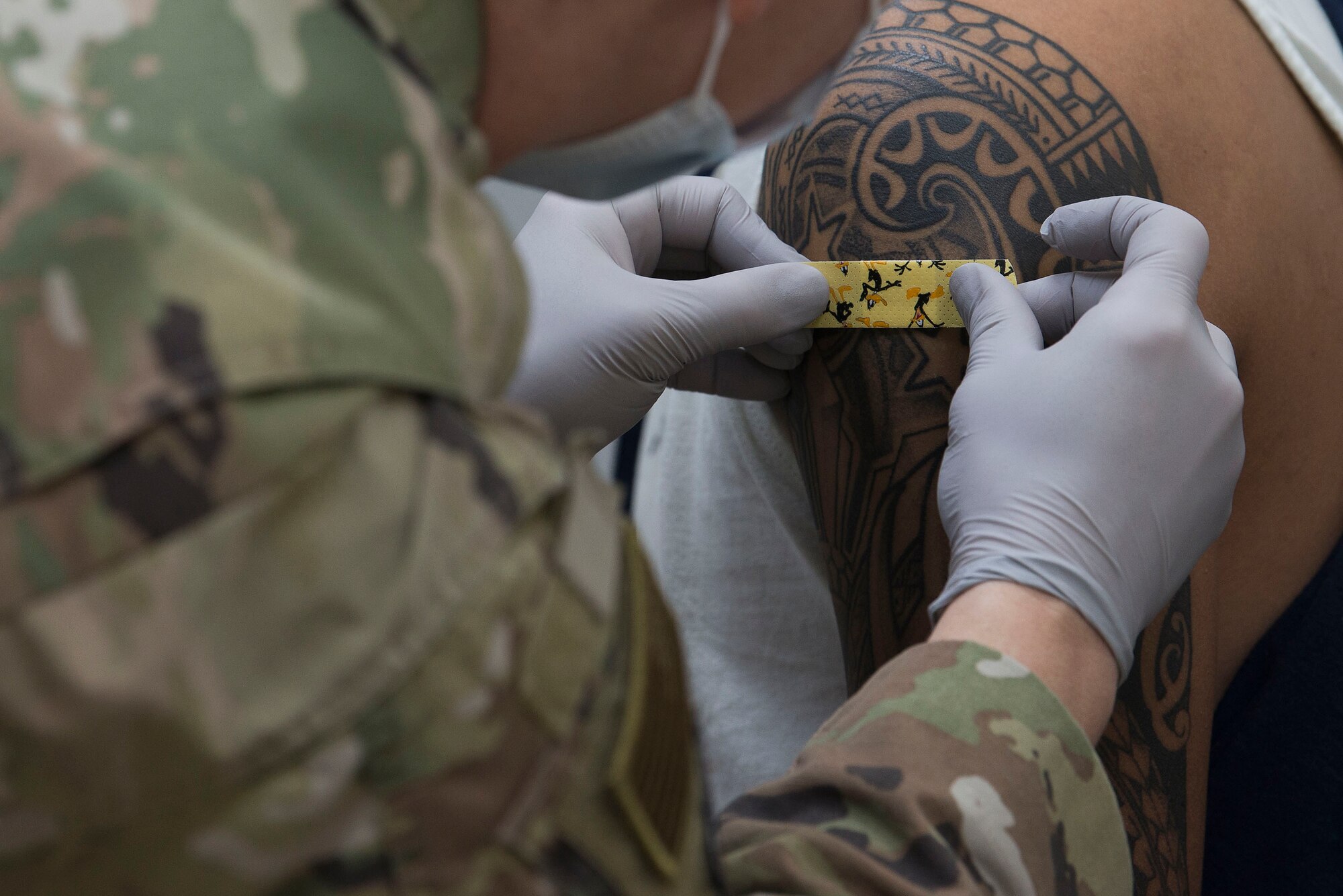 A medical technician assigned to the 380th Expeditionary Medical Group (EMDG) applies a bandage to a 380th EMDG clinic staff member following administration of a voluntary COVID-19 vaccine at Al Dhafra Air Base (ADAB), United Arab Emirates, Jan. 24, 2021.