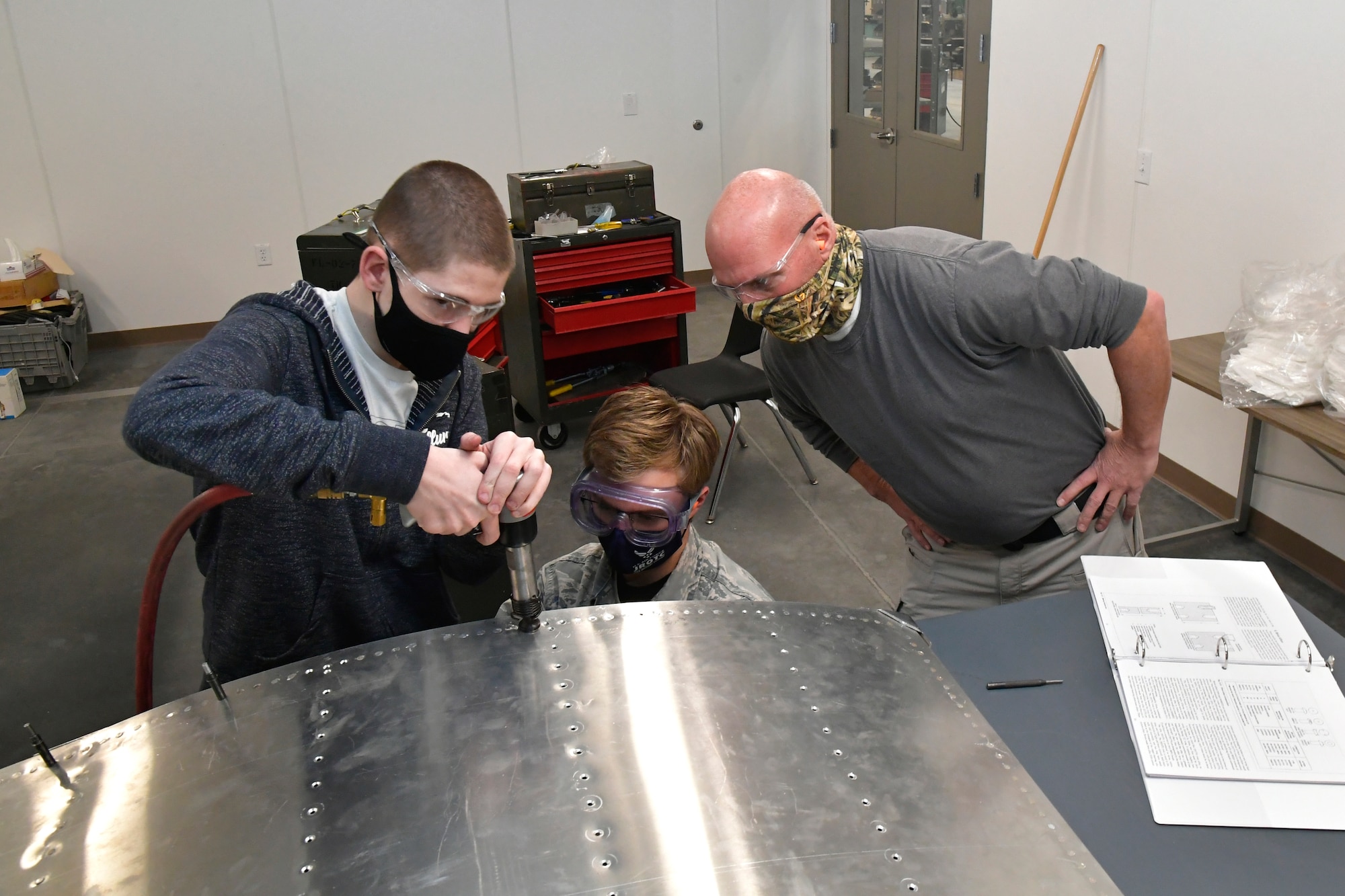 (Left to right) Isaac Jensen and Connor Innocenzi, both Utah Military Academy students, are taught proper riveting technique on part of an aircraft fuselage skin by Darrel Gronau, aviation structure repair instructor.