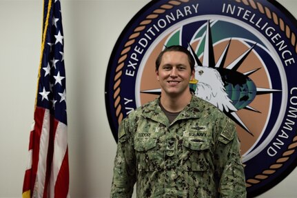 Intelligence First Class Todd Egdorf, pictured in front of a command logo, received a Meritorious Unit Commendation (MUC) award during the ceremony at navy Expeditionary Intelligence Command (NEIC).