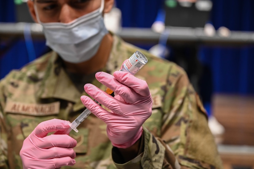 An airman wearing a face mask and gloves prepares a COVID-19 vaccine.