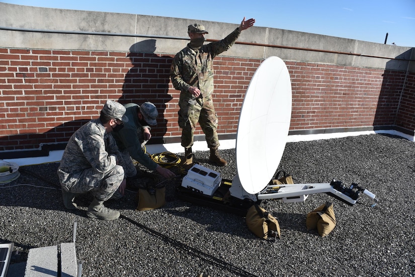 Three soldiers set up a satellite dish.