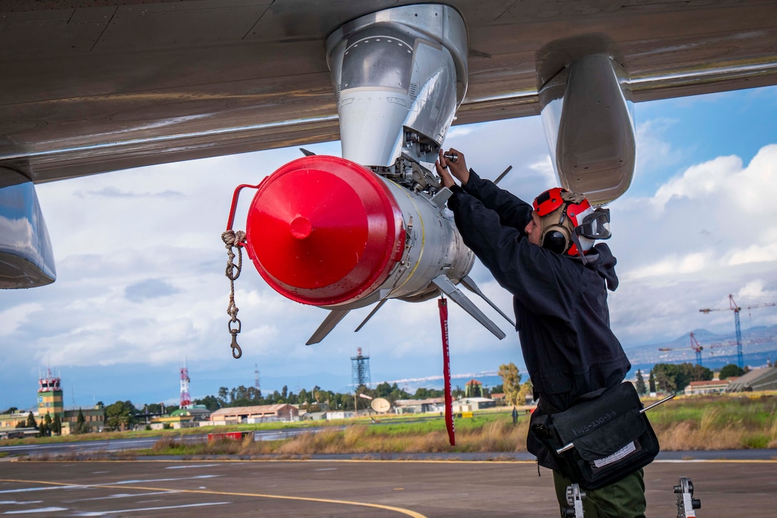 A sailor uses tools to work on a missile attached to a Navy aircraft.