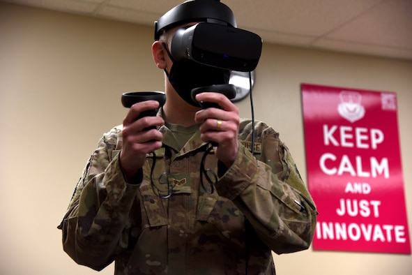 An Airmen holds joysticks and uses a virtual reality headset to test contacting software inside of the Innovation Lab.