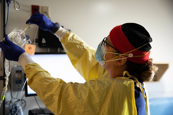 A nurse wearing personal protective equipment prepares intravenous medication for a patient.