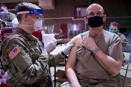 Alaska Army National Guard Spc. Alexander Martin-Frank, a combat medic with the Alaska Army National Guard Medical Detachment, administers the first dose of the COVID-19 vaccine Jan. 24, 2021, to Warrant Officer candidate Charles Hooper at Joint Base Elmendorf-Richardson. The detachment is administering the vaccine to Alaska National Guard members on a voluntary basis.