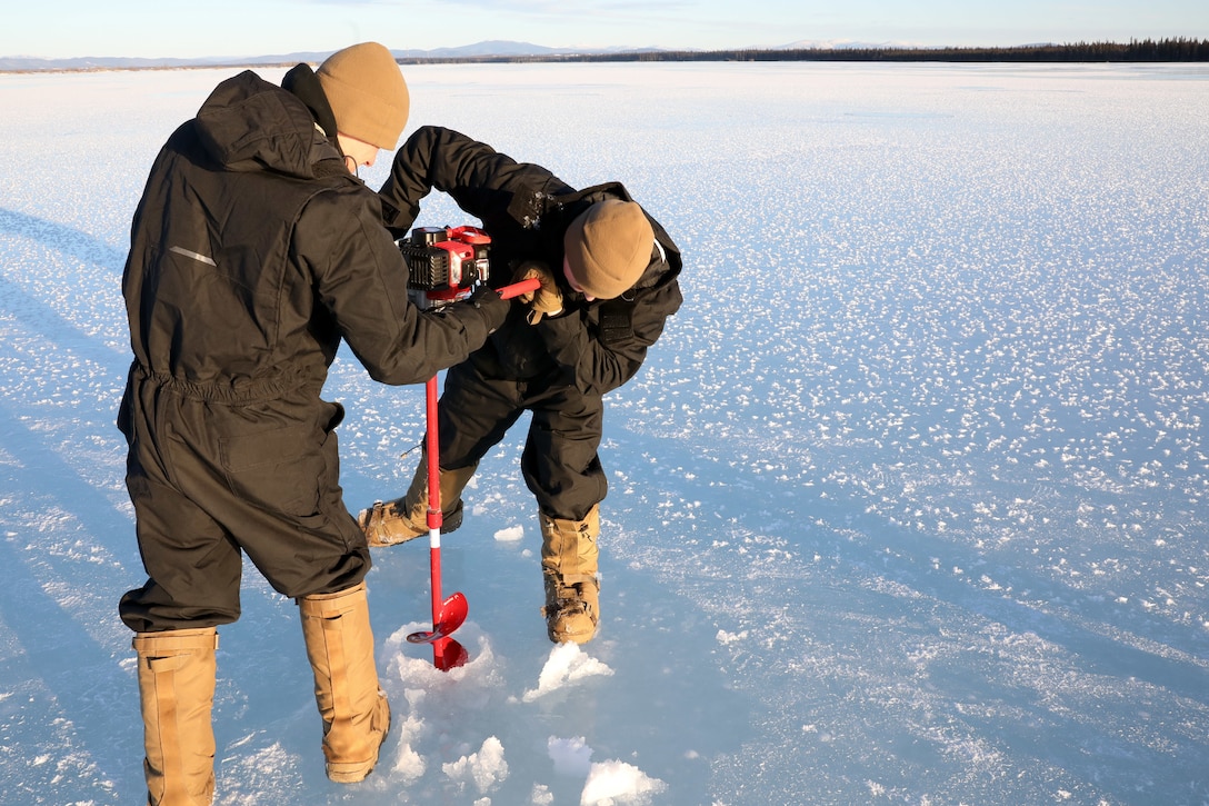 Two people use a drill to make a hole in the ice.