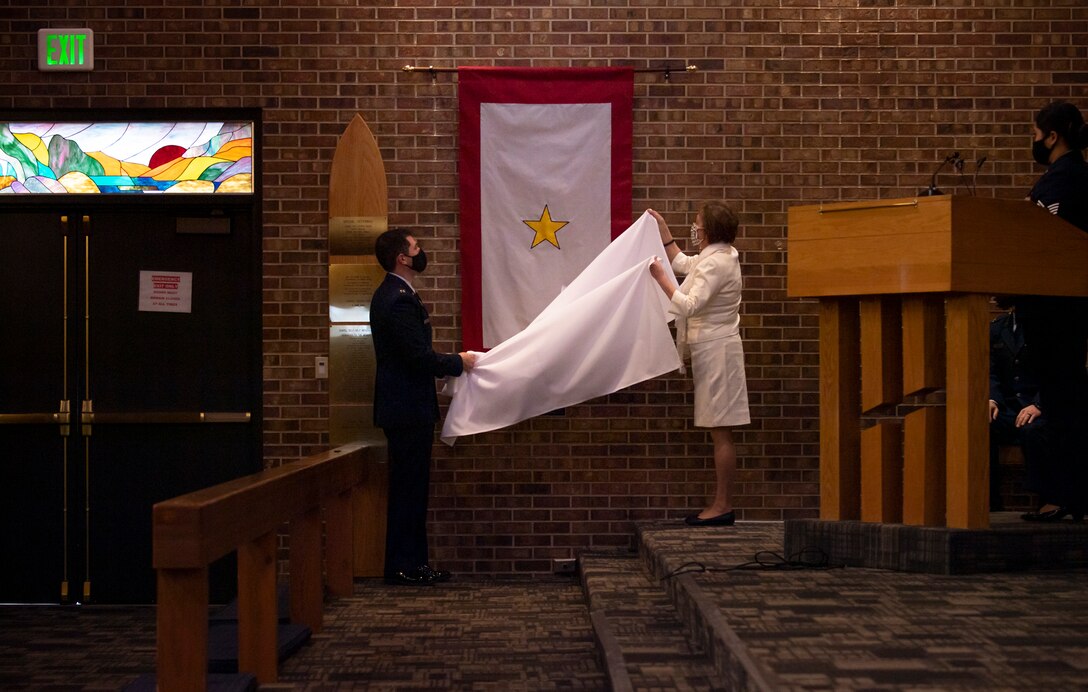 U.S. Space Force Capt. Nathaniel Lee and Kliffa Hall unveil a Gold Star flag Jan. 25, 2021, inside the Peterson-Schriever Garrison Chapel at Peterson Air Force Base, Colorado. Lee and Hall are Gold Star family members, Lee the son of U.S. Army Capt. Donald Lee and Hall the mother of U.S. Air Force Capt. Ryan Hall. During the dedication ceremony, Gold Star family members representing all services spoke on the personal impact of the Gold Star program.