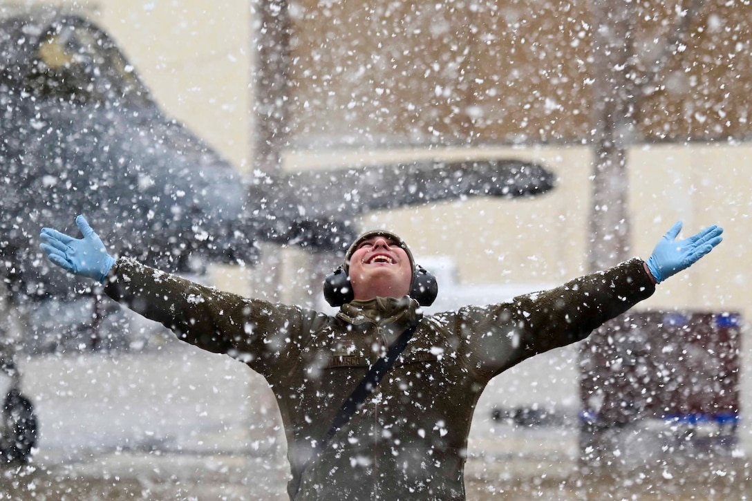 A smiling airman stands with arms outstretched as snow falls.