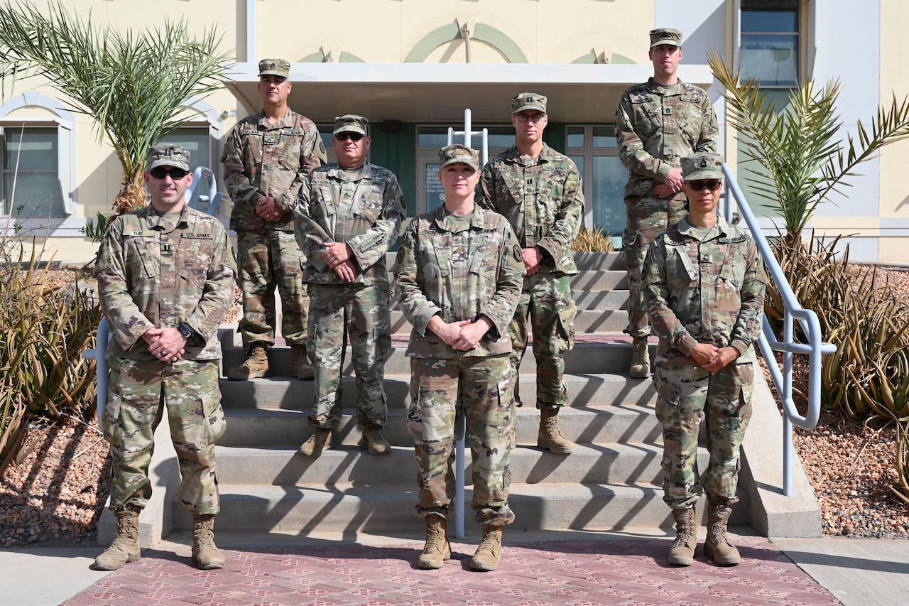 Seven soldiers stand spaced out on steps outside a building.