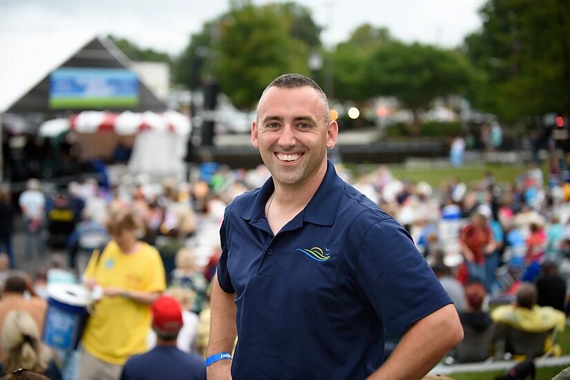 A man with hands on his hips smiles.A crowd is blurred out behind him.