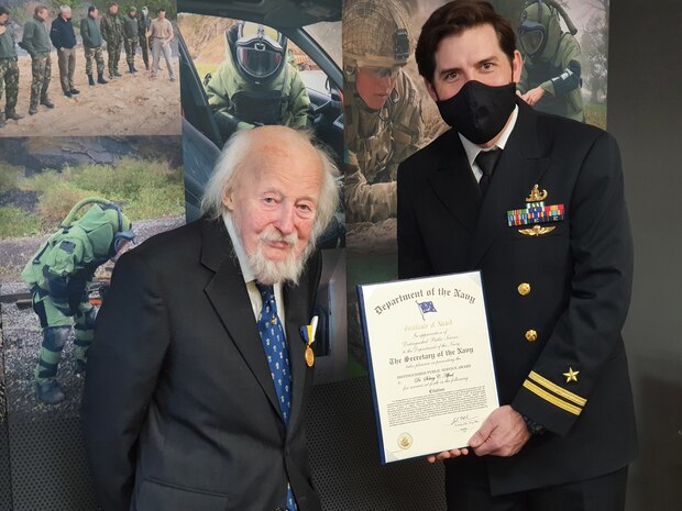 Dr. Sidney Alford (left) is presented the Department of the Navy Distinguished Public Service Award by Lt. Stephen Honan (right), an exchange officer at the Defense Explosive Ordnance Disposal (EOD) School, during the Winter EOD Technology and Training Program Board Meeting at Naval Surface Warfare Center Indian Head Division, Jan. 26. Alford has been a significant contributor to the joint service EOD community throughout the Department of Defense for more than 25 years and has put his inventions and life on the line to support EOD personnel. (U.S. Navy photo/released)