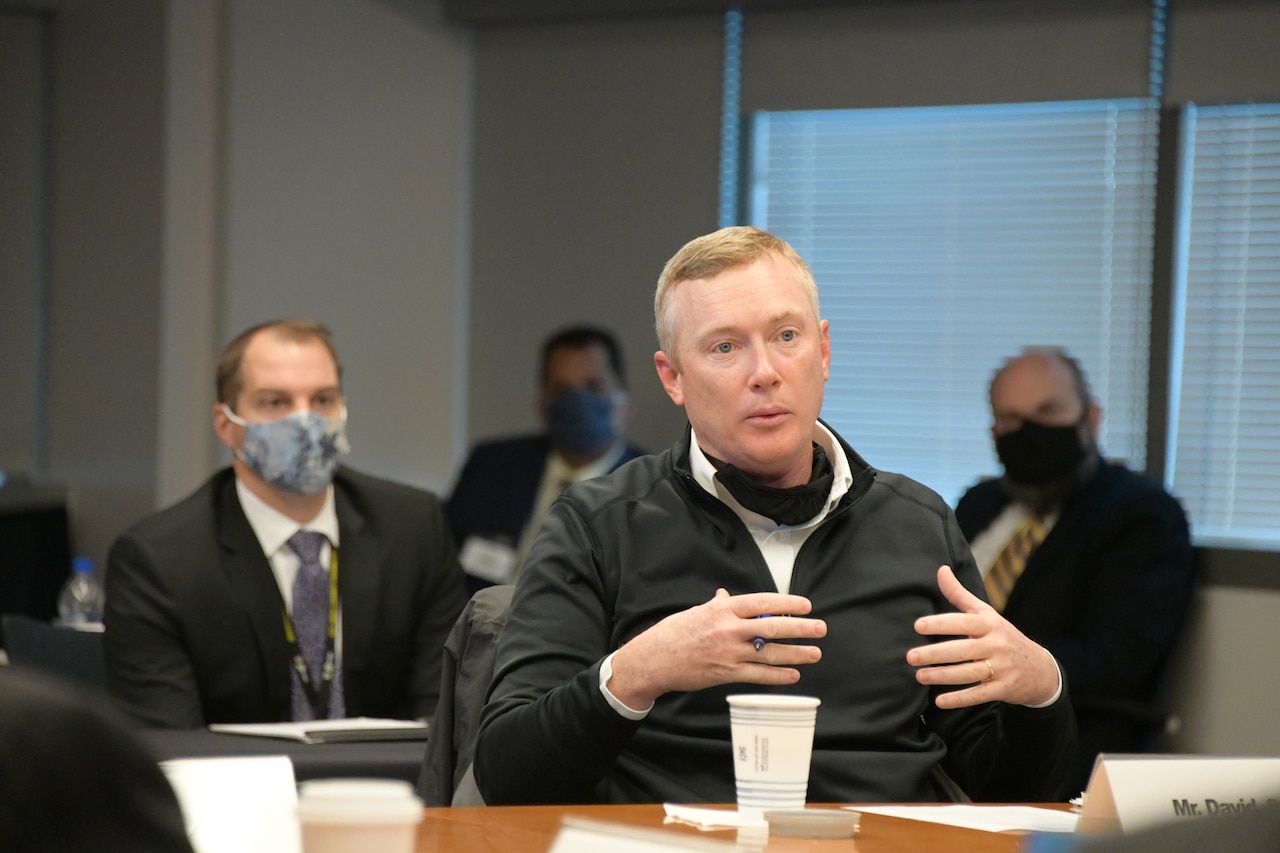 A civilian, seated at a table, speaks.