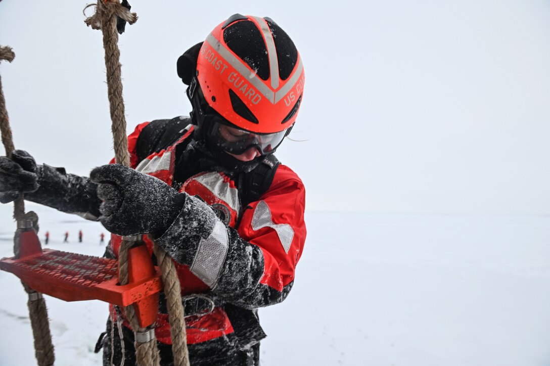A Coast Guardsman climbs a ladder while wearing an ice suit.