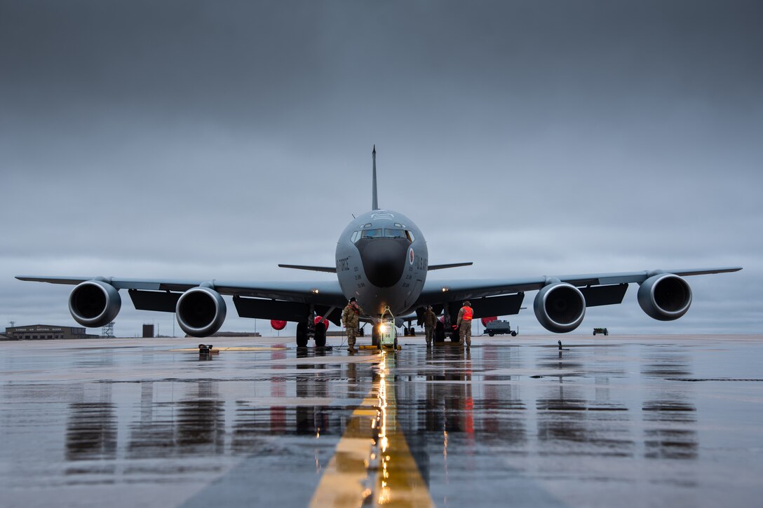 Three airmen stand on a wet runway next to a large aircraft.