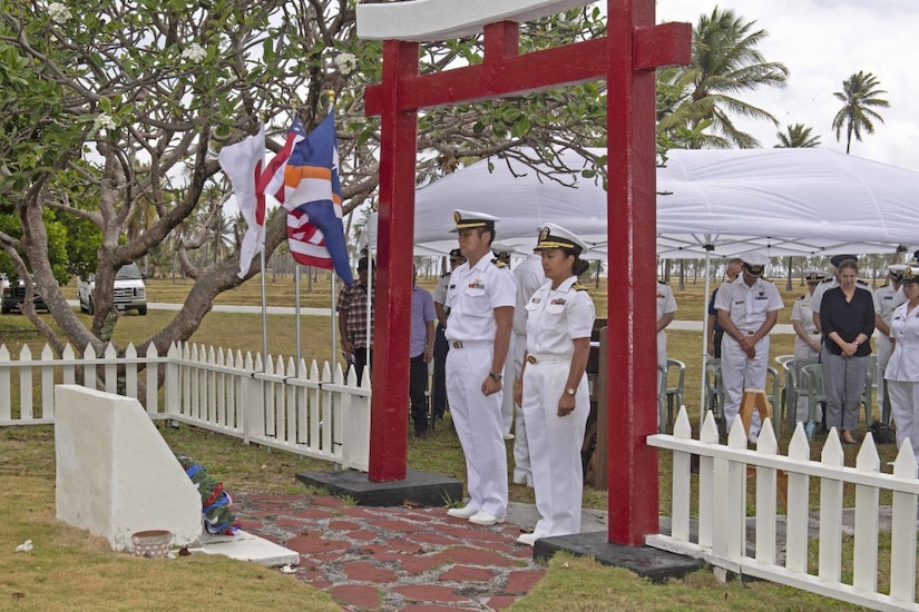 Two sailors stand at attention in front of a gravesite.