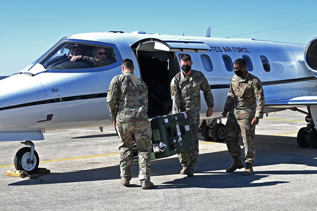 Three Air Force airmen wearing face masks carry doses of COVID-19 vaccines off an Air Force C-21 Learjet shortly after landing
