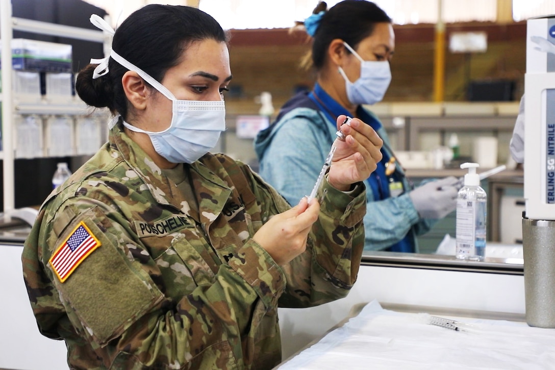 Two soldiers wearing face masks and gloves standing next to each other, prepare COVID-19 vaccines.