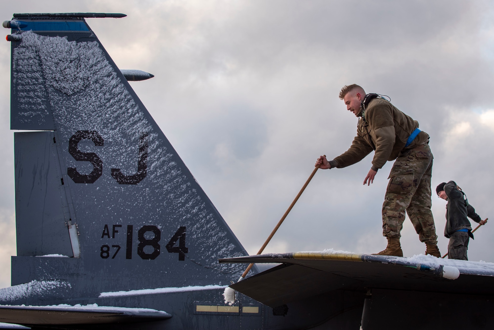 Senior Airman Collin Melton, 334th Aircraft Maintenance Unit avionics technician (front), and Senior Airmen Nicholas Verinder, 334th AMU avionics technician (back), clean snow off of an F-15E Strike Eagle at Seymour Johnson Air Force Base, North Carolina, Jan. 28, 2021.