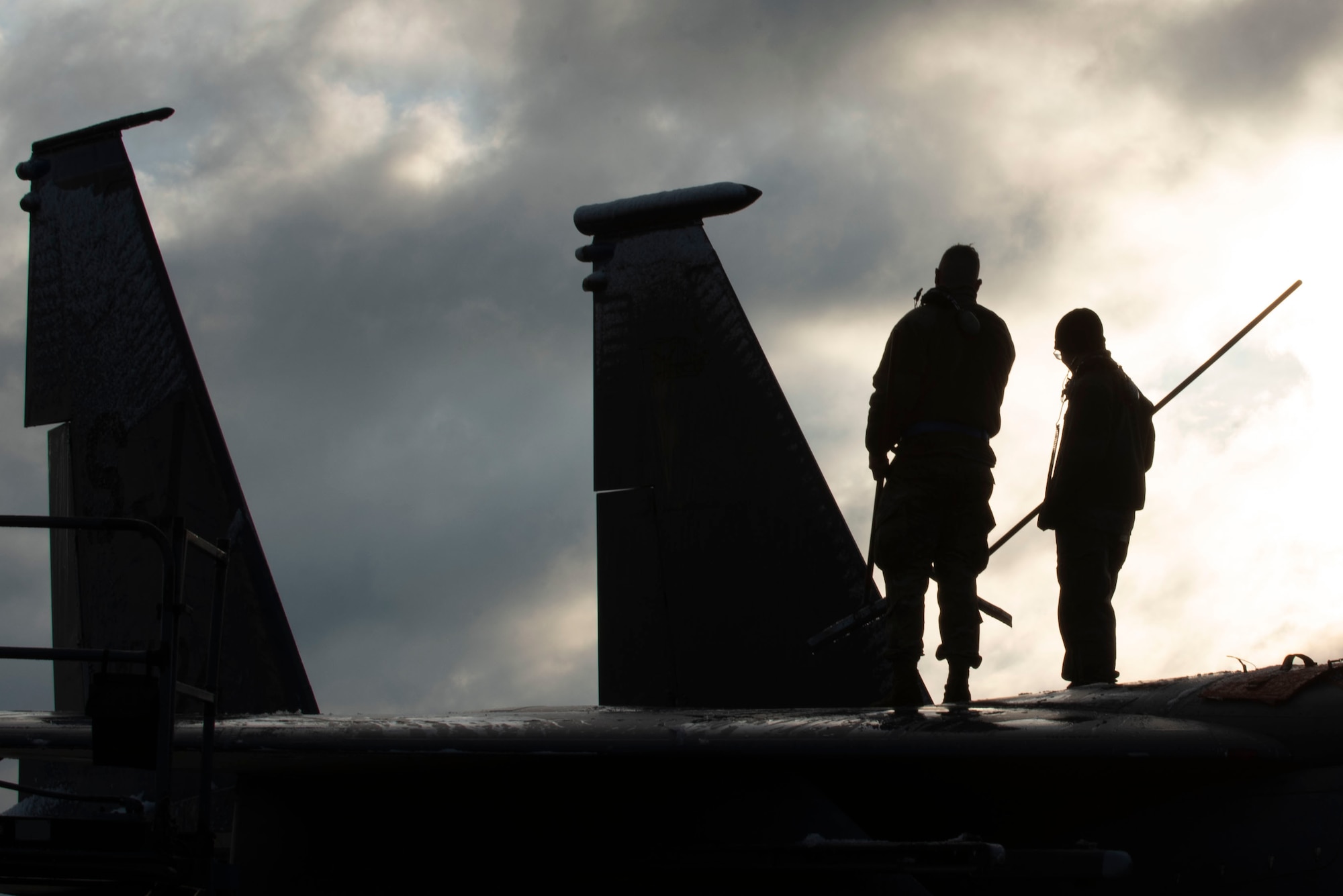 Senior Airman Collin Melton, 334th Aircraft Maintenance Unit avionics technician (left), and Senior Airmen Nicholas Verinder, 334th AMU avionics technician (right), clean snow off of an F-15E Strike Eagle at Seymour Johnson Air Force Base, North Carolina, Jan. 28, 2021.