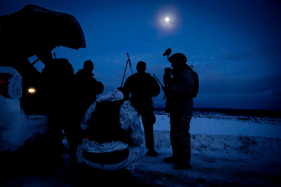 Marines and National Guard soldiers shown in silhouette stand in a circle at night.