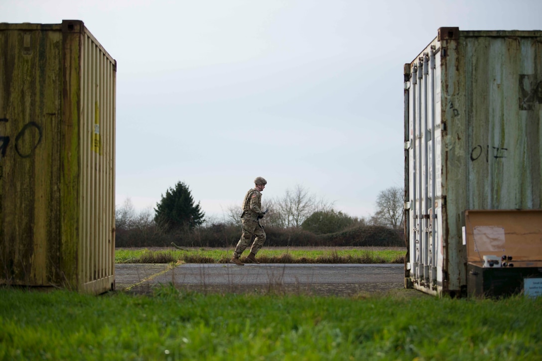 A soldier runs in between two shipping containers.