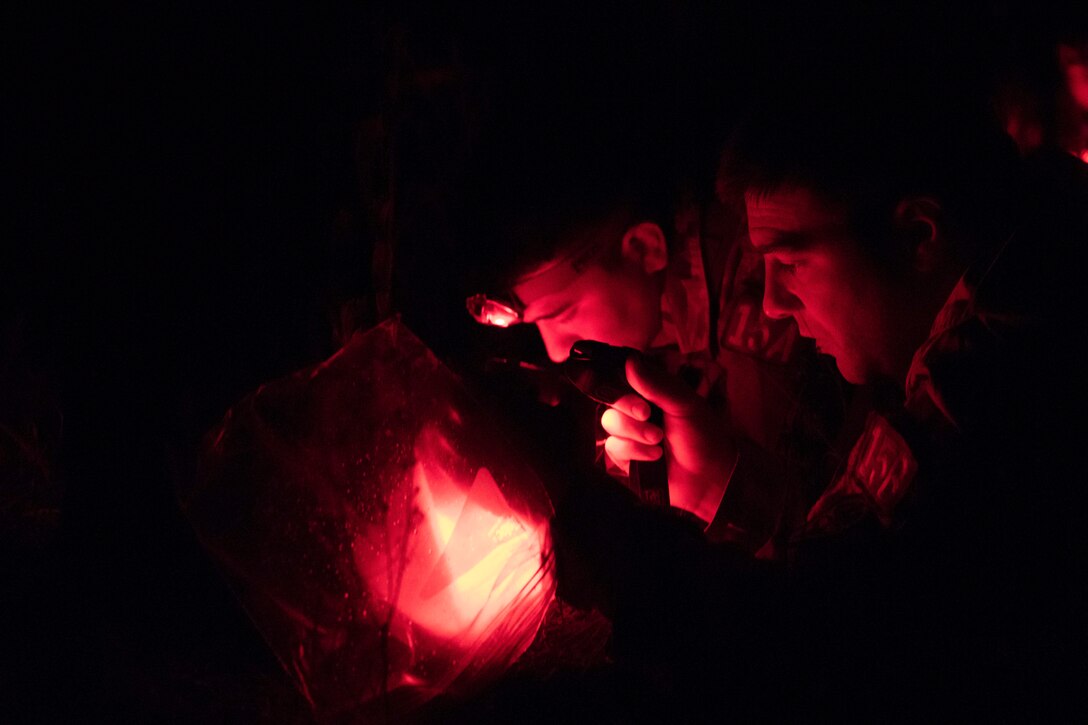 Soldiers look at a map at night illuminated by red light.