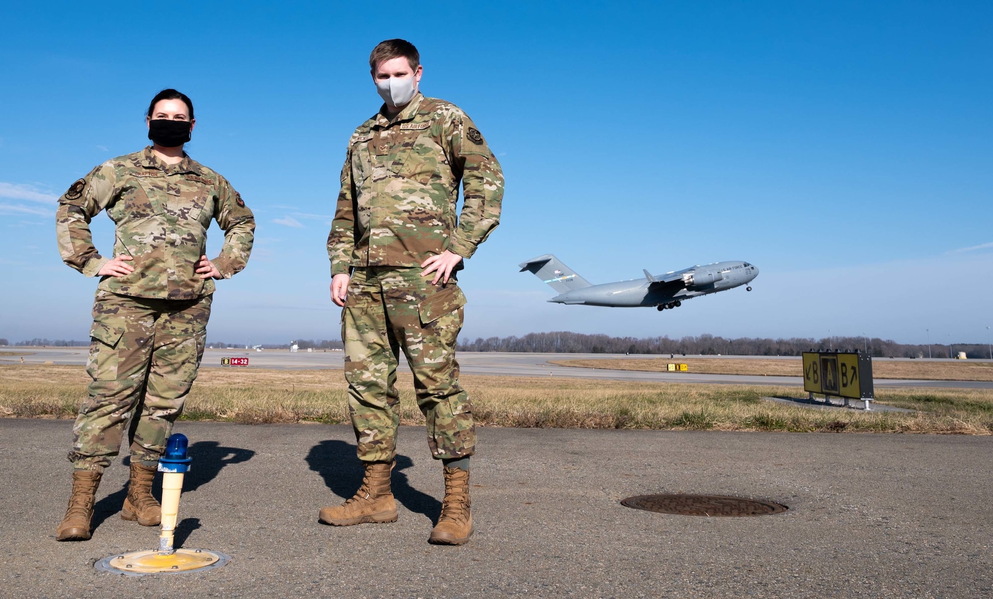 Senior Airman Kristina Grafton, 436th Operations Support Squadron airfield management operations supervisor, and Senior Airman Keyton Nickell, 436th Airfield Operation Support Squadron airfield management shift lead pose for a photo as a C-17 Globemaster III departs Dover Air Force Base, Delaware, Jan. 14, 2021. After the delayed launch of Total Force Training Records, Grafton built a digital training tracker, which was distributed to 133 other bases by the Air Force Flight Standards Agency as the airfield management career field’s interim standard for training documentation. (U.S. Air Force photo by Airman 1st Class Faith Schaefer)