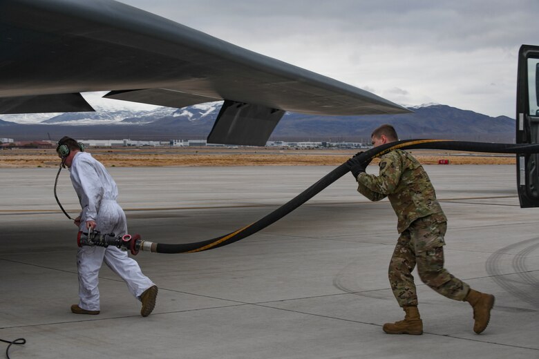 U.S. Air Force Tech. Sgt. Jimmy Womac, left, 393rd Expeditionary Bomb Squadron crew chief, and Senior Airman Christopher McLane, right, 6th Logistics Readiness Squadron fuels technician, run a fuel hose to a B-2 Spirit Stealth Bomber during Red Flag 21-1, at Nellis Air Force Base, Nevada, Jan. 26, 2021. In order to ensure Whiteman always upholds its global deterrence responsibility, Red Flag challenged Airmen operate in a limited environment to better enhance their readiness and ensure mission success. (U.S. Air Force photo by Staff Sgt. Sadie Colbert)